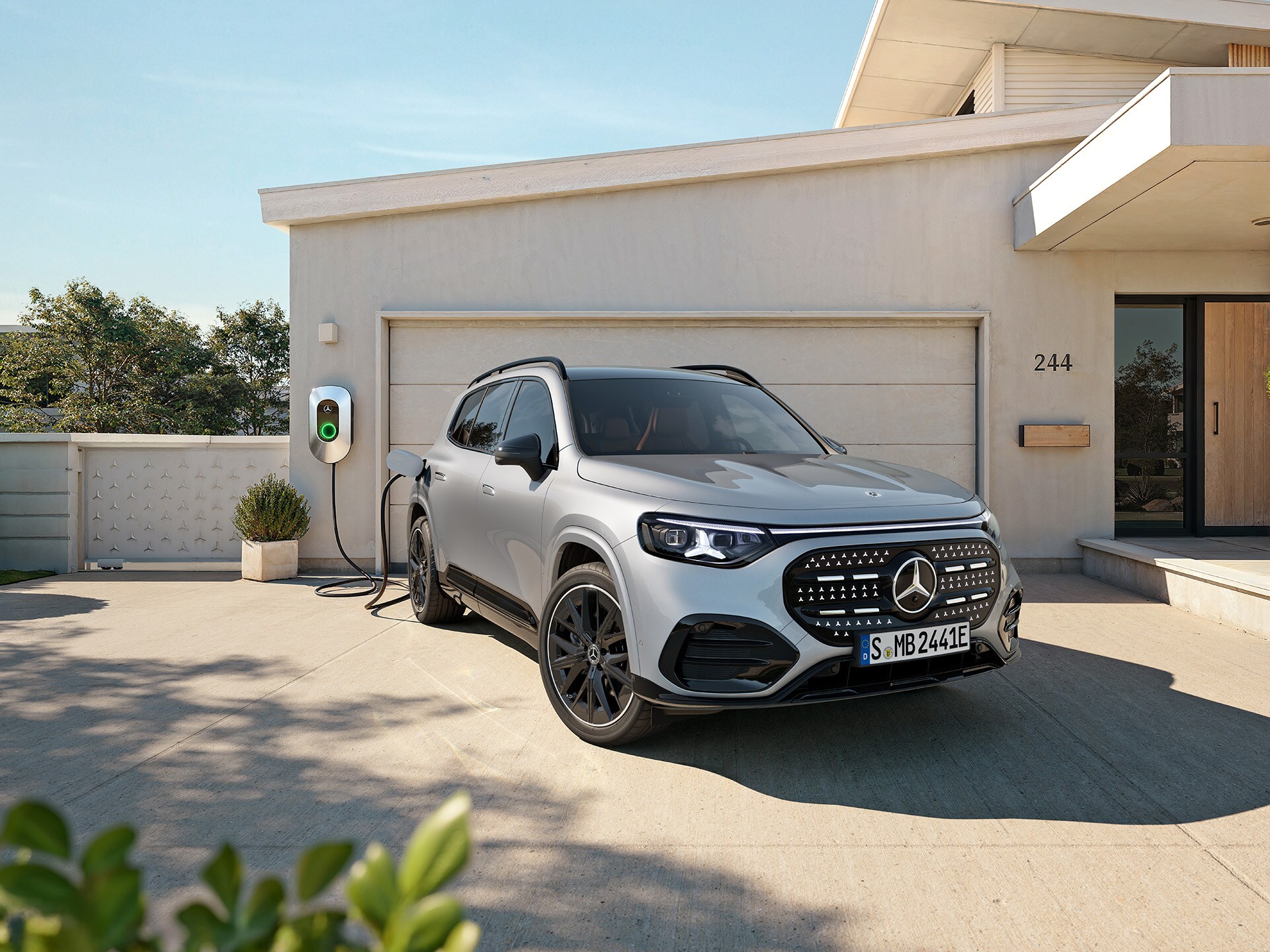 GLB 100% eléctrico | Mercedes-Benz La imagen muestra un GLB eléctrico gris enchufado al cargador y aparacado fuera de una casa