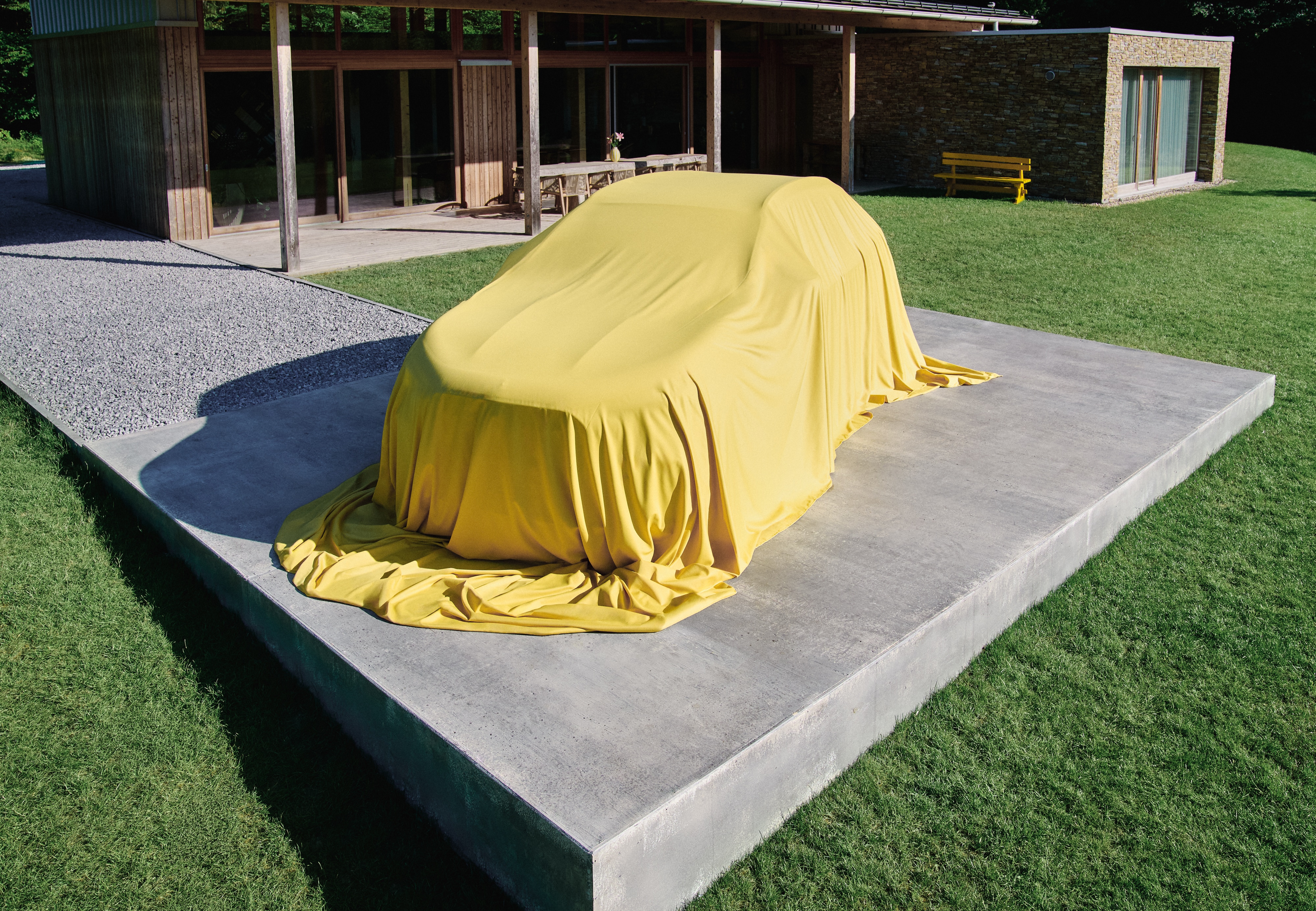 Visual del nuevo GLA cubierto con un velo amarillo frente a una casa.
