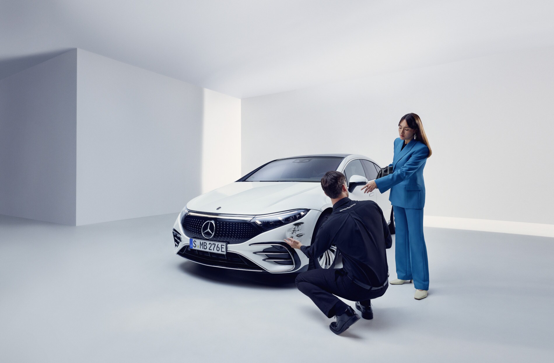 Reparación de daños | Mercedes-Benz Un integrante del equipo de asistencia de Mercedes-Benz arrodillado junto a un Mercedes-Benz averiado.