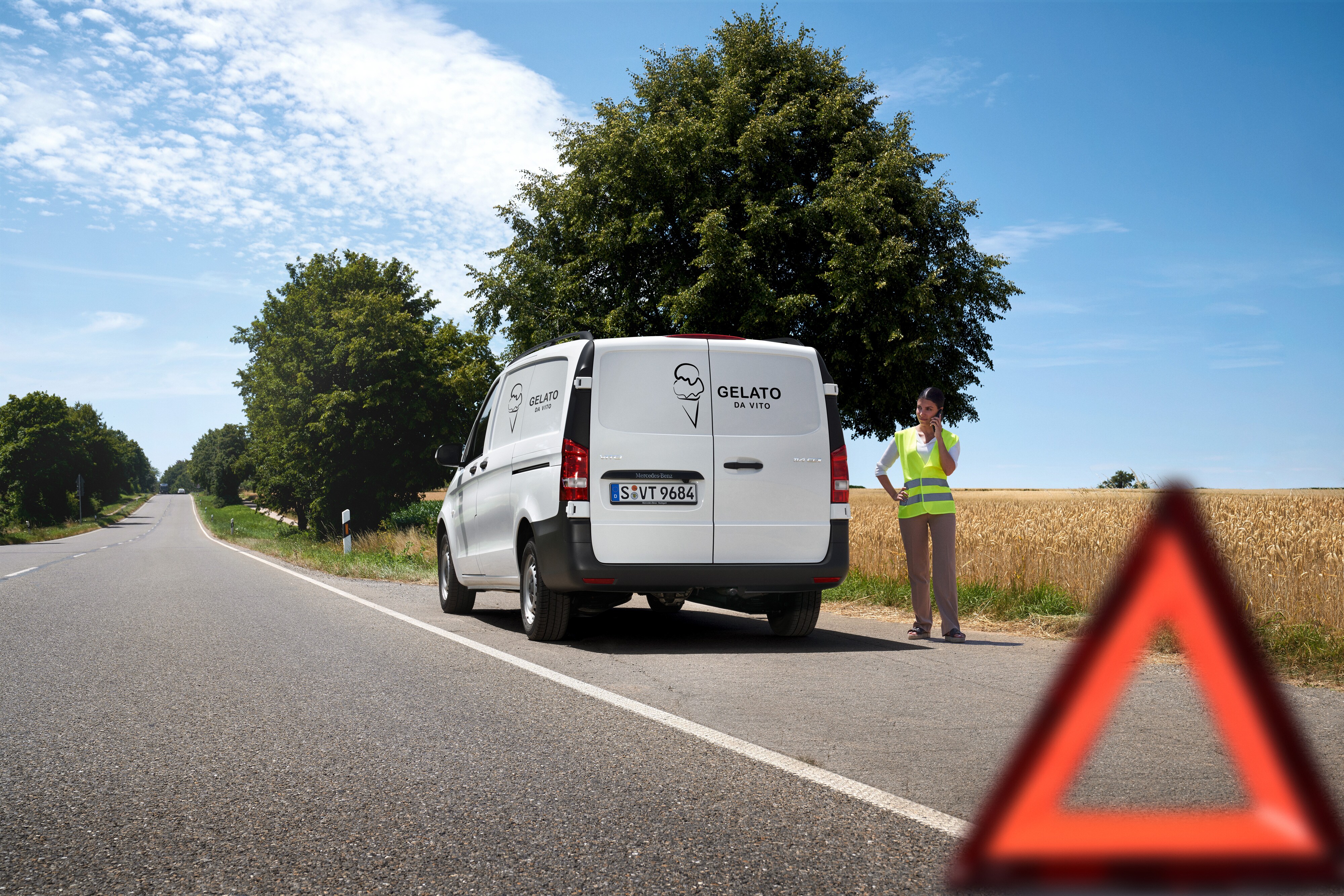 Mercedes-Benz | Vans Care | Service24h A woman calls the Mercedes-Benz service 24h hotline, a Mercedes-Benz Sprinter is stationary by the side of country road.