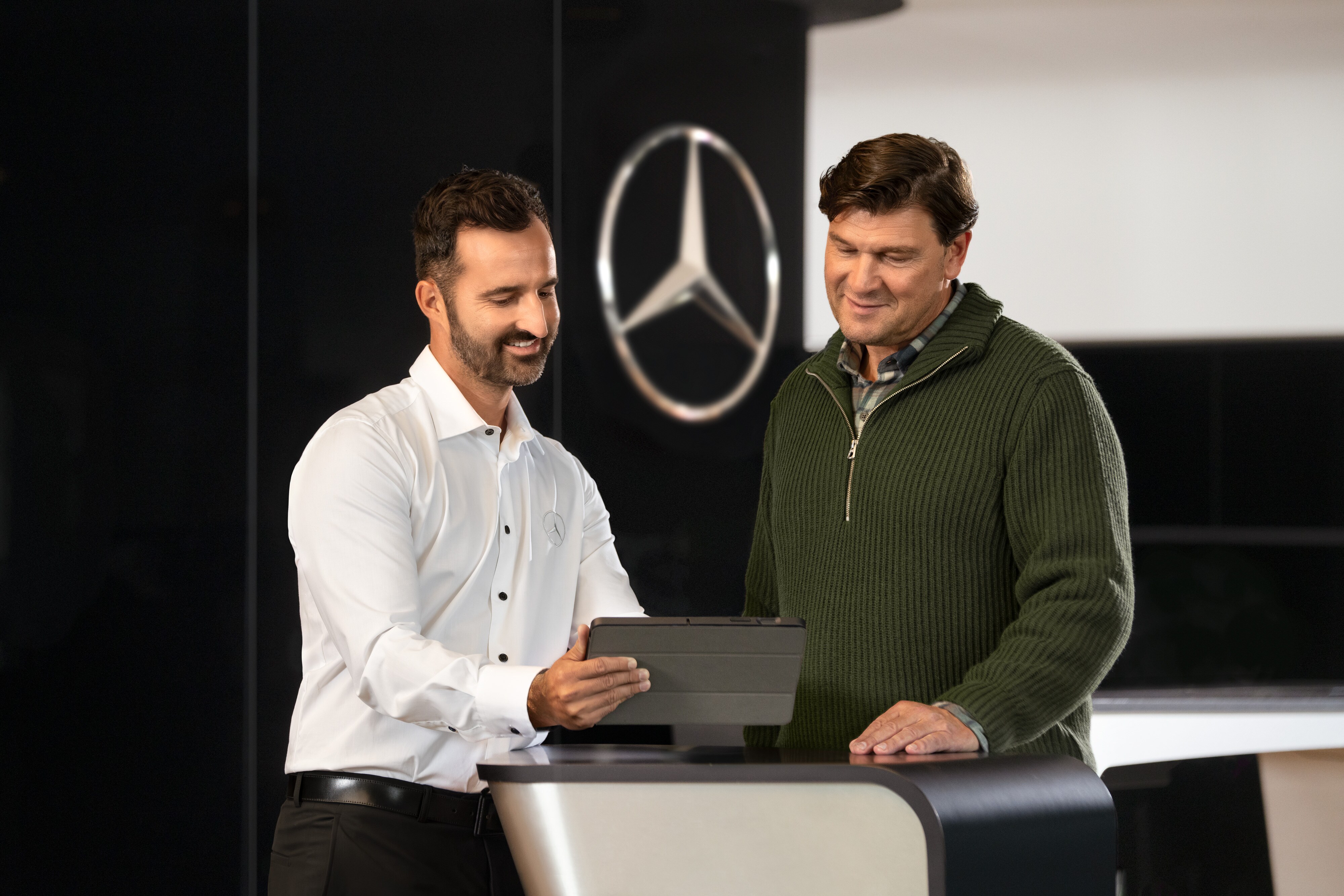 Mercedes-Benz | Servicios de un vistazo Dos hombres conversando en un mostrador y mirando una tablet, delante de la estrella de Mercedes-Benz.