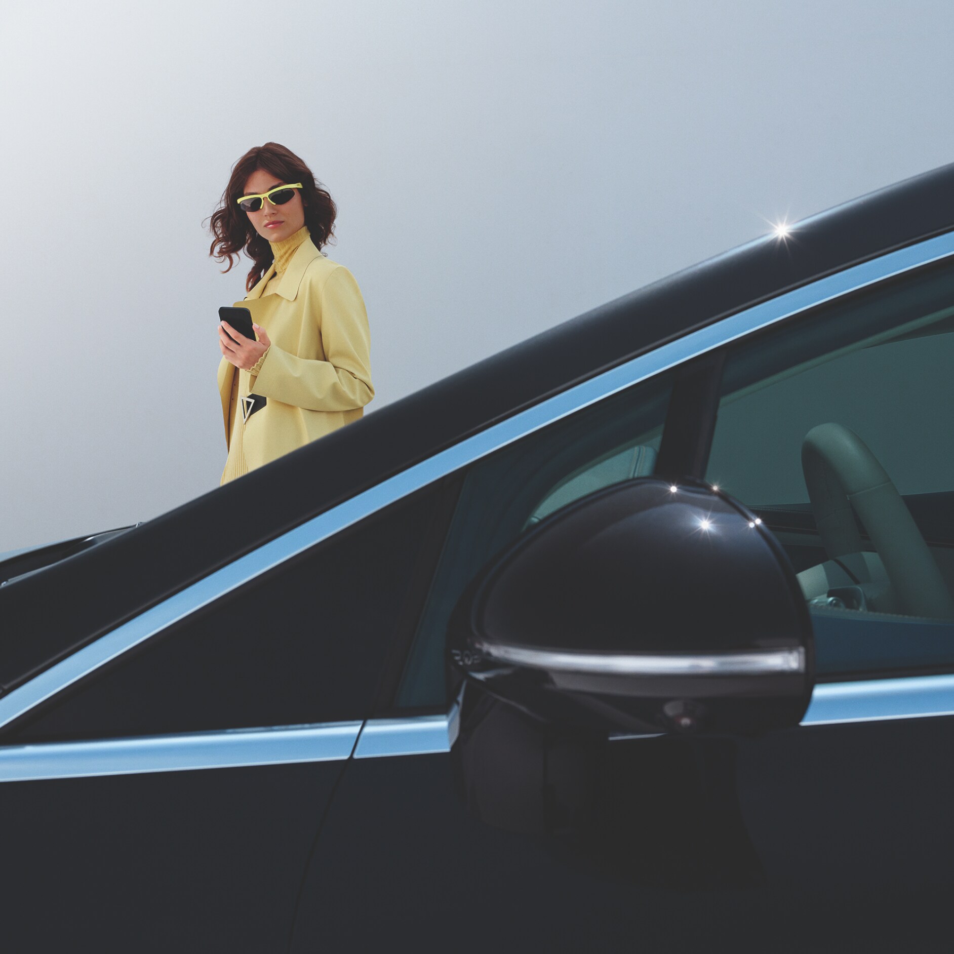 Mercedes-Benz | Oferta Cambio de Lunas visual de una mujer vestida de amarillo con gafas de sol detrás de un coche negro