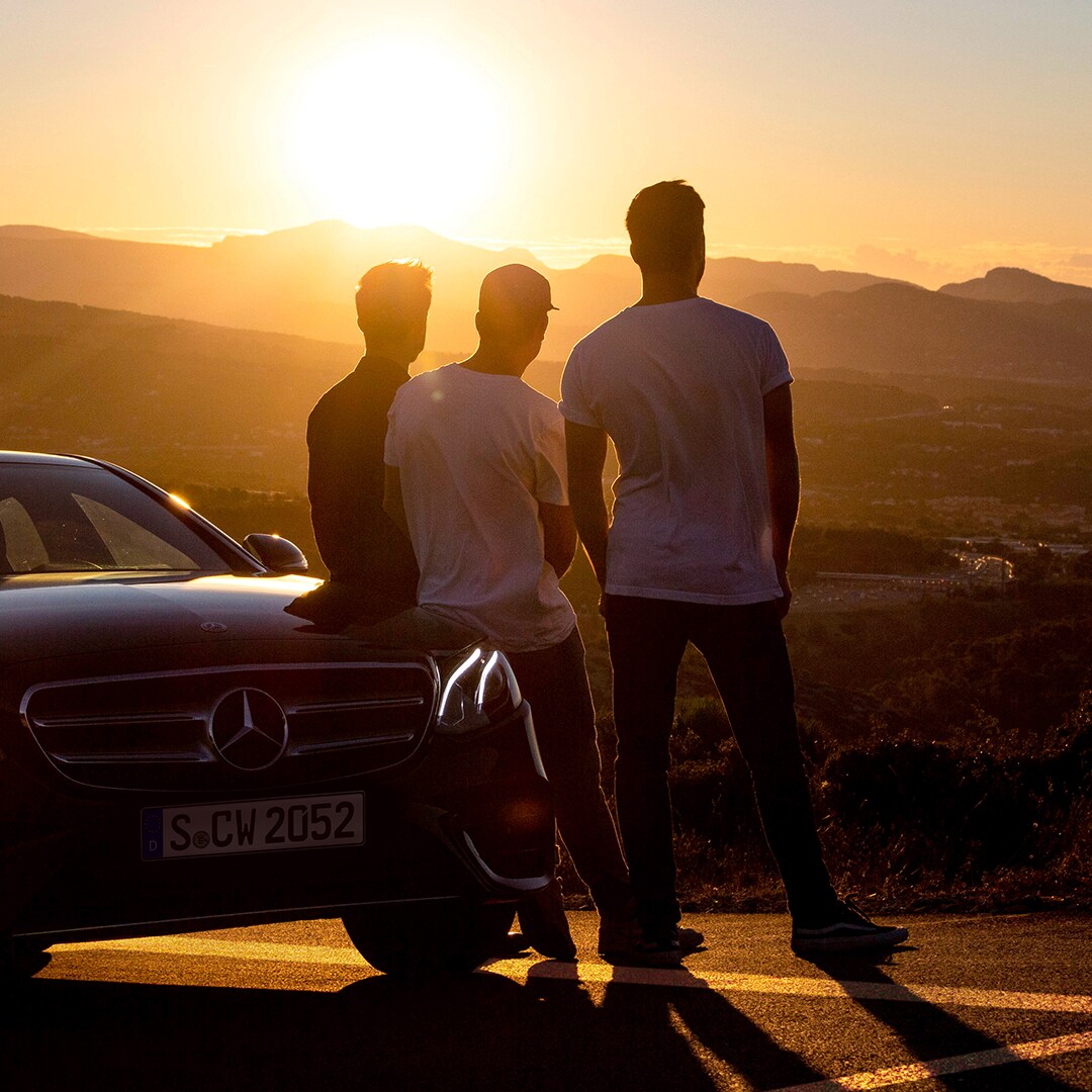 140 años de innovación | Mercedes-Benz Vista de tres hombres de espalda mirando el atardecer, apoyados en un Mercedes-Benz
