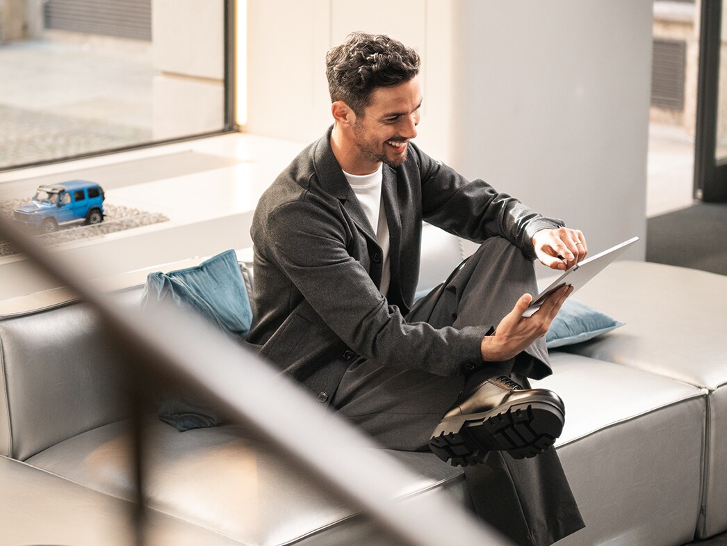 Portal del cliente | Servicios financieros | Furgonetas Mercedes-Benz Un hombre sonríe mientras usa una tableta en un sofá.